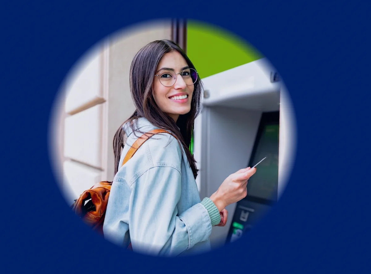 Person wearing a backpack uses an ATM while holding a bank card.