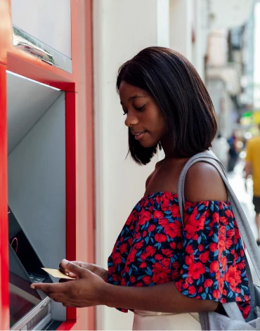 A person uses an ATM while holding a card near the screen.