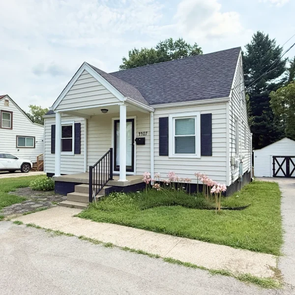 Exterior of a white single-story home with black shutters, a covered front porch and a detached garage.